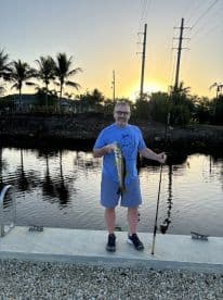 A man proudly displays his catch while fishing at sunset, showcasing the thrill of outdoor fishing experiences.