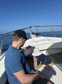 A father watches as his young child crawls on the deck of a boat, capturing a sweet family moment on the water.