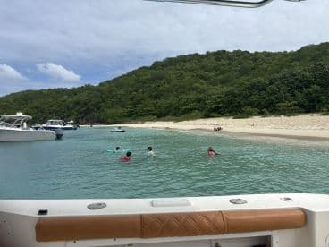 A group of children enjoys swimming in the clear waters near a sandy beach, with boats anchored nearby — a perfect sandbar stop for family fun.