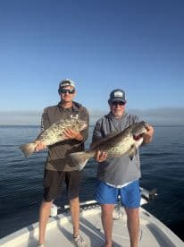 Two anglers proudly display their impressive catch while fishing on a boat, showcasing a successful day on the water.