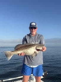 A proud angler displays a large grouper catch while fishing on a boat, showcasing the thrill of a successful day on the water.