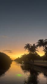 A stunning sunset over a tranquil canal, framed by palm trees, creating a picturesque scene perfect for evening boat rides or relaxation.