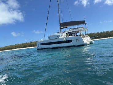 A stunning side view of a catamaran cruising through clear waters, showcasing its sleek design against a backdrop of lush greenery and sandy shores.