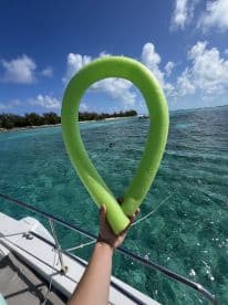 A vibrant green floating mat is held up against a stunning turquoise backdrop, showcasing the perfect day for water activities and relaxation on the boat.