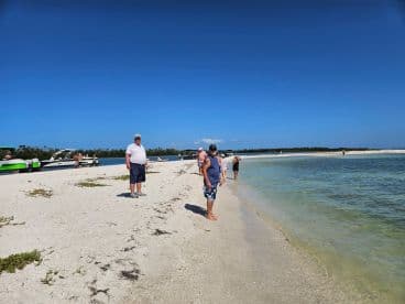 A group of people enjoys a sunny day at the beach, with boats anchored nearby, perfect for a sandbar stop and relaxation.