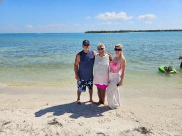 A cheerful group poses on the beach, enjoying a sunny day by the water, with swimming and relaxation in the background — perfect for family outings and beach days.
