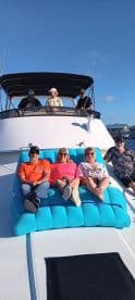 A lively group enjoys a sunny day on the boat, relaxing on a vibrant blue lounge while sipping drinks — perfect for a fun day out on the water.