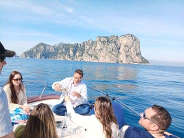 A lively group enjoys drinks on a boat with stunning coastal scenery in the background, perfect for celebrations and memorable outings on the water.