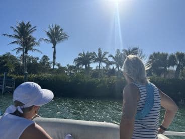 Two women enjoy a scenic boat ride surrounded by lush palm trees and bright sunshine, capturing the essence of a perfect day on the water.