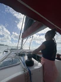 A sailor actively maneuvers the ropes on a sailboat, showcasing the excitement of sailing on open waters under a beautiful sky.