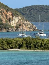 A picturesque view of boats anchored in a serene harbor, surrounded by lush greenery and rocky cliffs — a perfect destination for sailing enthusiasts.