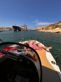 A couple enjoys a relaxing day sunbathing on the bow of a boat in a picturesque harbor, perfect for unwinding and soaking up the sun.