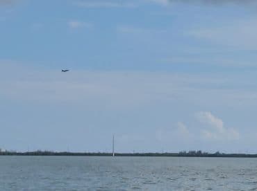 An unclear image featuring a plane flying above a body of water, with distant land visible in the background.