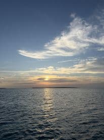 A serene sunset over calm waters, with distant islands silhouetted against the colorful sky — an ideal backdrop for a peaceful evening on the boat.