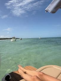 A relaxing scene featuring a person's feet resting on the edge of a boat, with a beautiful turquoise sea and other boats in the background — perfect for a day of leisure on the water.