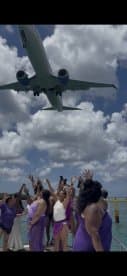A lively group celebrates on a boat as an airplane flies overhead, capturing the excitement of a fun day on the water.
