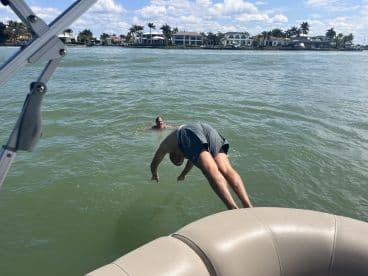 A person dives off a pontoon boat into the water while another swims nearby, capturing the essence of fun and adventure on the water.