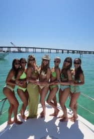 A lively group of friends poses together on a boat, celebrating in stylish swimwear against a stunning turquoise backdrop — perfect for bachelorette parties or summer getaways.
