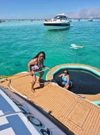 Two friends enjoy a sunny day on the water, with one preparing to jump into a floating pool while the other relaxes. This vibrant scene captures the essence of summer fun and relaxation on a boat.