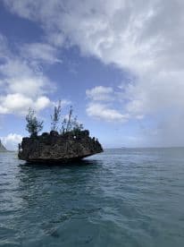 A rocky formation surrounded by water under a cloudy sky, creating a serene coastal scene.