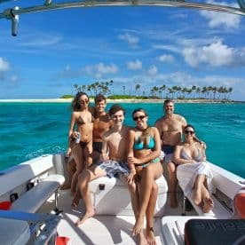 A cheerful group enjoys a sunny day on a boat, surrounded by stunning turquoise waters and a picturesque island backdrop — perfect for memorable beach outings.
