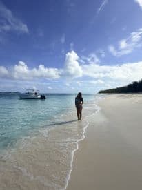 A woman enjoys a serene moment on the beach, with a boat anchored nearby, capturing the essence of a perfect island getaway.