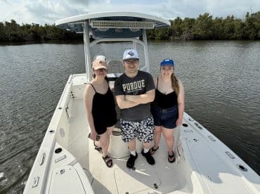 A group of friends poses on the deck of a boat, enjoying a day on the water surrounded by lush greenery — perfect for memorable outings and adventures.