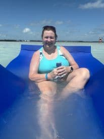 A woman enjoys a relaxing moment on a floating mat in shallow waters, perfect for summer fun and group gatherings.