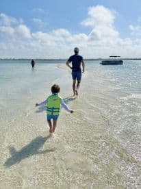 A joyful family moment as a child in a life jacket runs along the shallow water towards a boat, creating unforgettable memories on a sunny beach day.