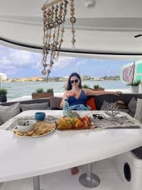A woman enjoys a refreshing cocktail while seated at a beautifully arranged table with snacks and fruits on a luxurious boat, perfect for a relaxing day on the water.