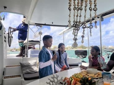 A lively scene inside a boat's cabin where children enjoy snacks and drinks while an adult steers the vessel — perfect for family outings on the water.