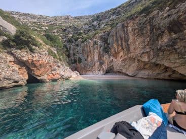 A picturesque cove with crystal-clear waters, where two people enjoy swimming while a boat is anchored nearby — a perfect spot for relaxation and exploration.