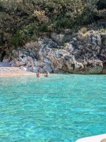 A couple enjoys a refreshing swim in crystal-clear waters near a rocky beach, perfect for a relaxing day in nature.