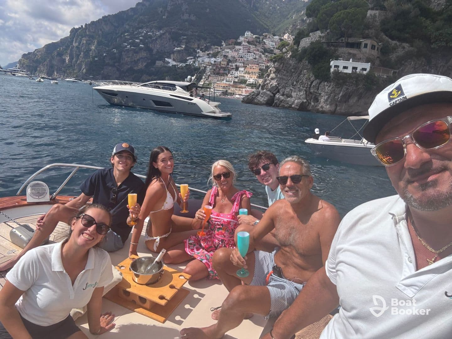 A lively group enjoys cocktails on a yacht, celebrating under the sun with stunning coastal views in the background — perfect for memorable outings on the water.