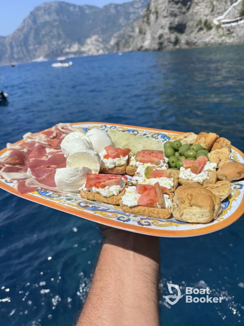 A delicious charcuterie platter featuring a variety of snacks, perfect for enjoying on a boat trip amidst stunning coastal views.