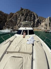 A woman enjoys sunbathing on the deck of a yacht, surrounded by stunning rocky cliffs and clear waters — a perfect scene for relaxation and adventure.