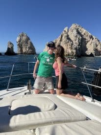 A couple shares a romantic moment aboard a boat in Cabo San Lucas, with stunning rock formations in the background — perfect for memorable getaways and celebrations.