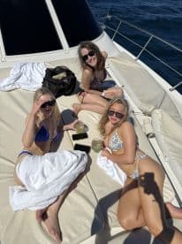 Three friends enjoy cocktails and sunbathe on the deck of a yacht, capturing the essence of a perfect day on the water.