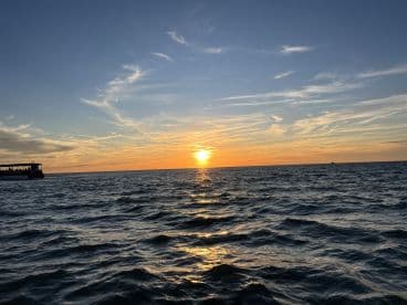 A stunning sunset over the ocean with a boat silhouetted against the vibrant sky, capturing the essence of a perfect evening on the water.