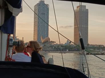 A couple shares a romantic moment aboard a sailboat during sunset, with a stunning cityscape in the background — perfect for intimate sailing experiences.