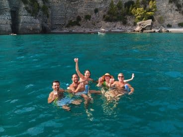 A lively group enjoys a refreshing swim in crystal-clear waters, raising their drinks in celebration — perfect for summer adventures and fun on the water.