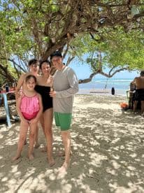 A joyful family poses together on the beach, capturing a memorable moment under the trees — perfect for family vacations and beach outings.