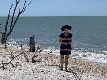 A woman stands on a serene beach, enjoying the sunny day with the ocean waves gently lapping at the shore — a perfect moment for relaxation and exploration.