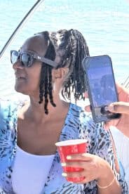 A joyful moment captured on a boat, featuring a woman enjoying a drink while another guest takes a photo — perfect for celebrating special occasions on the water.