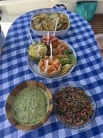 A vibrant spread of snacks including chips, guacamole, salsa, and a colorful fruit platter, perfect for enjoying on a boat trip.