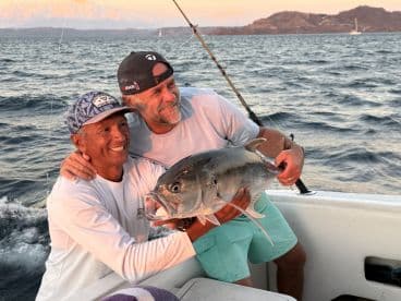 Two friends celebrate a successful fishing catch aboard a boat, showcasing the thrill of fishing adventures on the water.