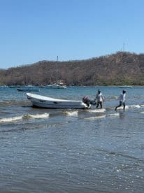 Two individuals are seen interacting with a boat in shallow water, showcasing the vibrant atmosphere of a coastal adventure.