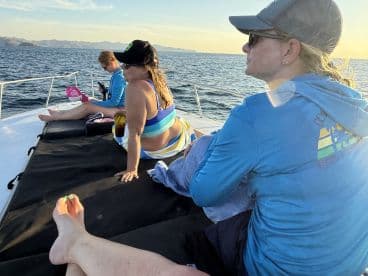 A group of friends relaxes on the deck of a boat, enjoying the sunset over the ocean — a perfect moment for unwinding and taking in the beautiful scenery.