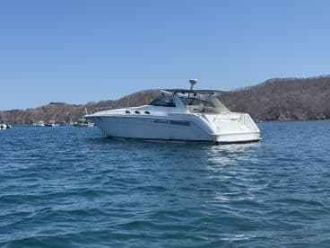 A sleek yacht cruising through clear waters, showcasing its elegant design against a scenic backdrop of hills.