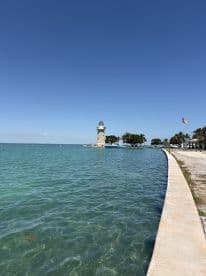 A scenic view featuring a lighthouse by the water, surrounded by clear turquoise waters and a bright blue sky.